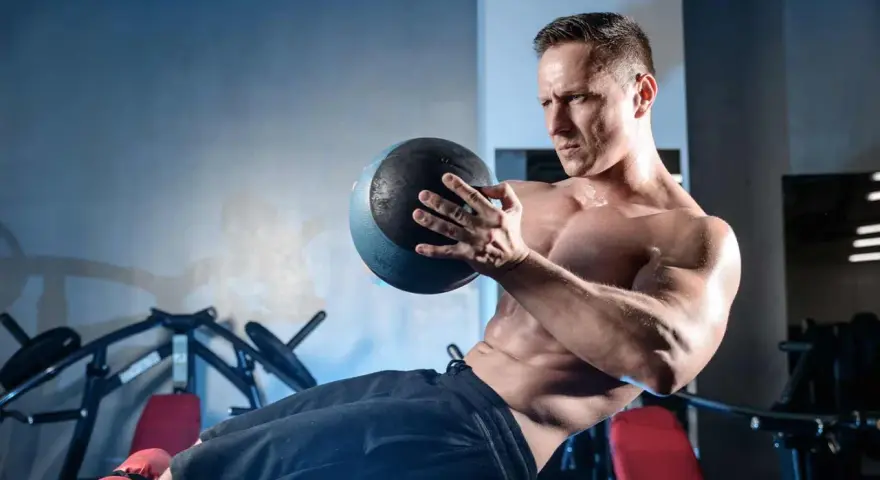 Un homme transpire en faisant un exercice oblique avec un ballon de médecine dans une salle de sport.