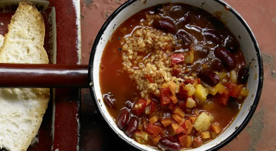 Herzhaftes Chili sin Carne mit Kidneybohnen, Bulgur und Gemüse in einem Topf, daneben geröstetes Brot.