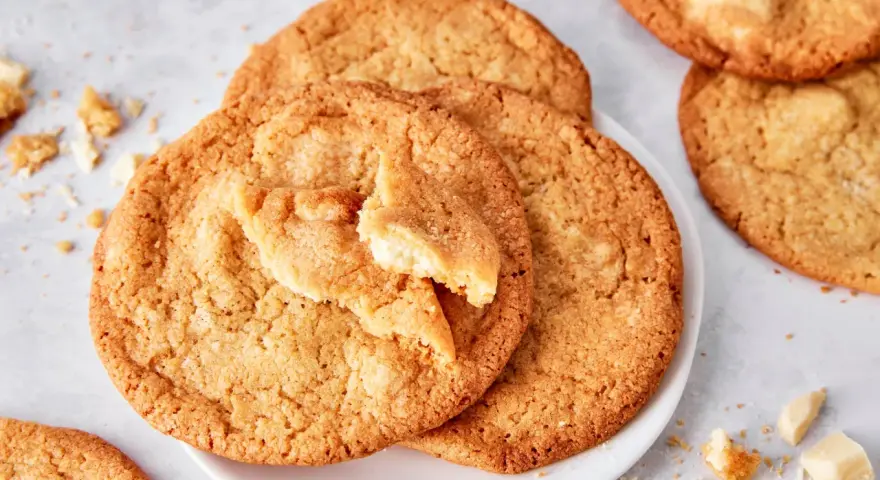 Saftige white chocolate cookies, eine davon angebrochen, mit Stückchen weißer Schokolade und Krümeln daneben.