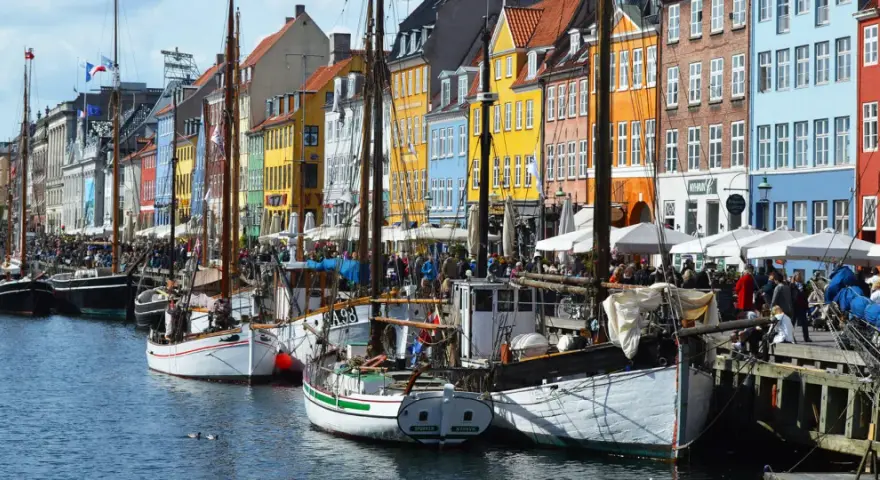 Colorful buildings line a canal in Copenhagen, with boats docked and people enjoying the waterfront. A perfect scene for exploring things to do in Denmark.
