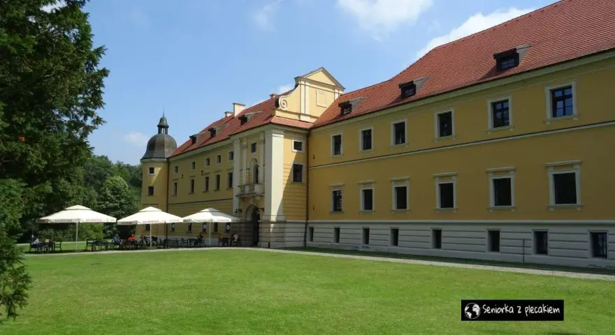 Żółty budynek opactwa cystersów w Rudach z czerwonym dachem i zielonym trawnikiem przed nim.
