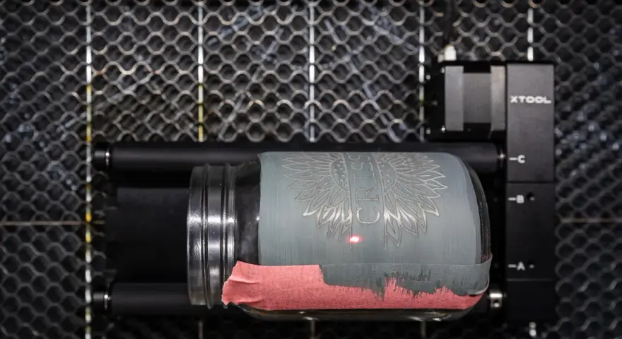 Laser engraving a jar with tempera paint. The laser is creating a sunflower design on the painted glass.