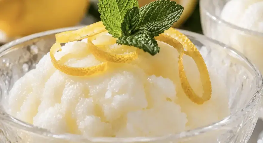 Sorbetto al limone senza albume, fresco e profumato, guarnito con scorzette di limone e foglioline di menta.