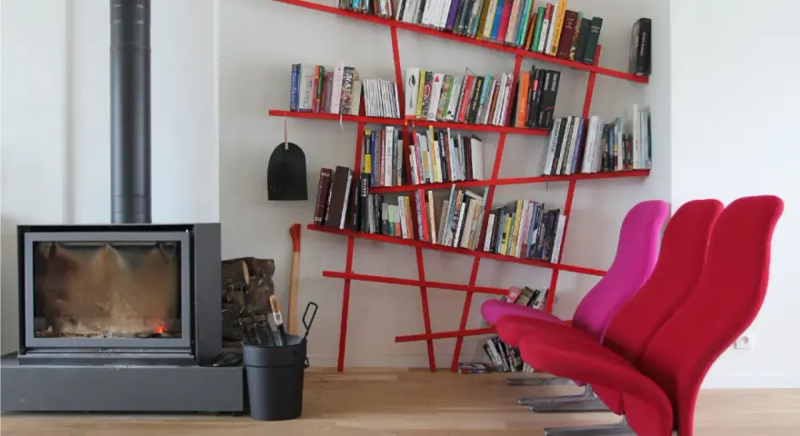 Camino acceso, attrezzi da camino, e moderne piccole librerie rosse piene di libri, con sedie colorate.