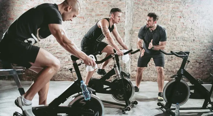 Trainer instructs men on stationary bikes. This workout can help build endurance, proving a stationary bike helps with running.