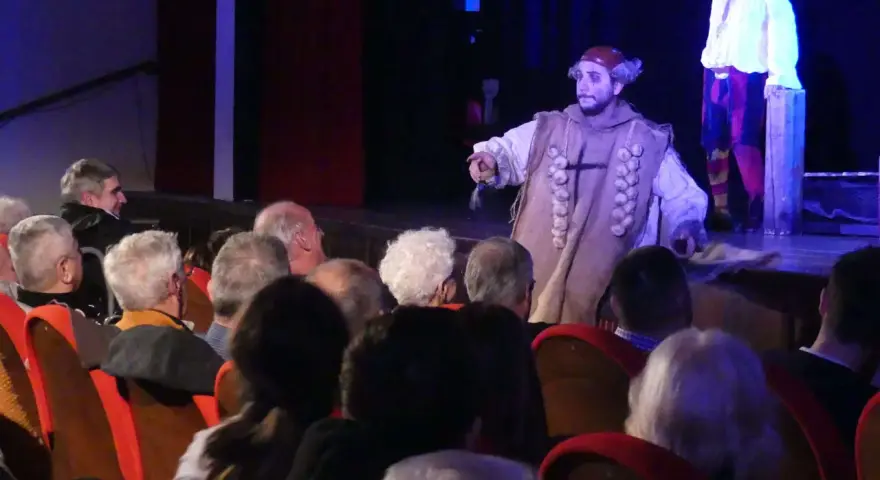Attori sul palco, uno con un costume particolare, sembrano rompere la **quarta parete significato** parlando al pubblico.