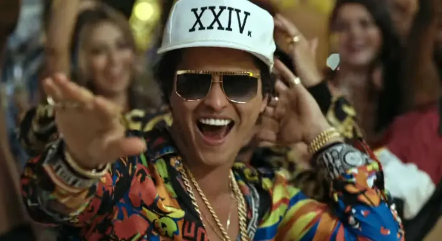 Bruno Mars w Polsce! Wesoły artysta w kolorowej koszuli i czapce z napisem "XXIV K" tańczy wśród rozbawionych ludzi.