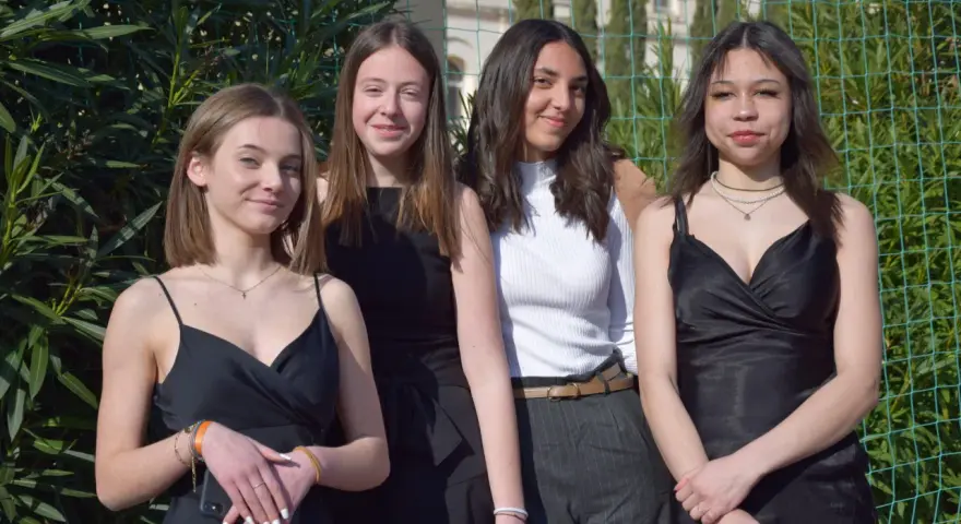 Quatre jeunes femmes posent, habillées élégamment. Idées pour comment s'habiller pour l'Aïd : robes noires, haut blanc chic, et accessoires discrets.