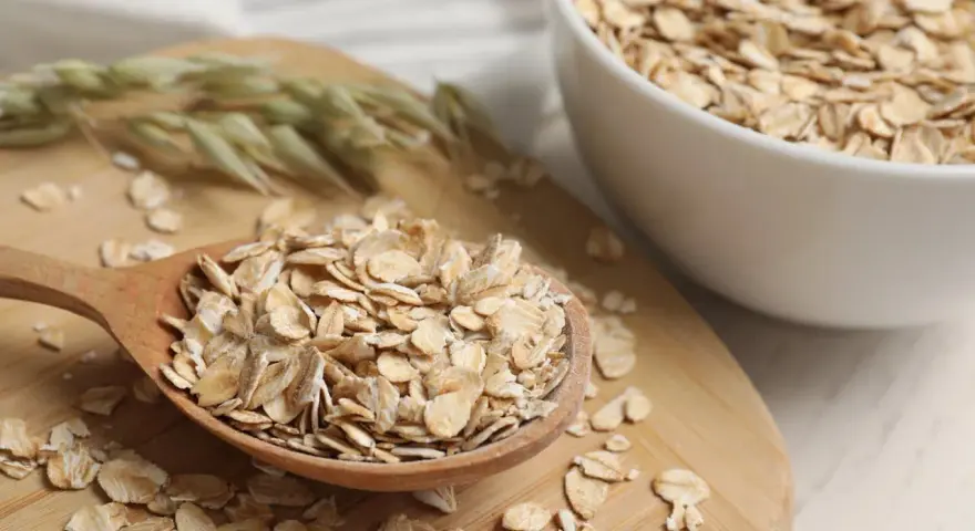 Płatki owsiane na drewnianej łyżce i w misce. Czy płatki owsiane mają gluten? Czysty owies jest bezglutenowy, ale warto sprawdzić etykietę.