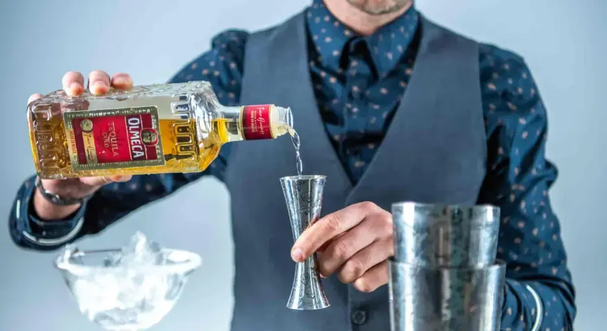 Barman nalewa Olmeca Tequila Gold do jiggera, idealna tequila do margarity. Obok kieliszek z lodem i shaker.