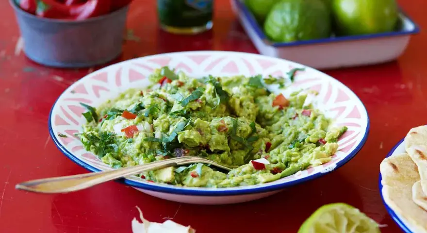 En skål med krämig guacamole, perfekt för ditt nästa guacamole recept. Serveras med tortillabröd, lime och chili.