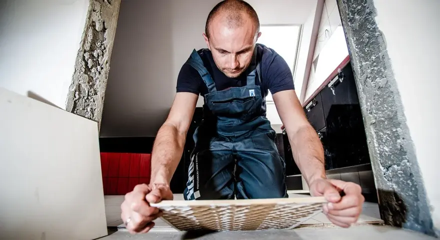 Remont trwa, a mężczyzna w ogrodniczkach zastanawia się, gdzie wyrzucić stare płytki ceramiczne.