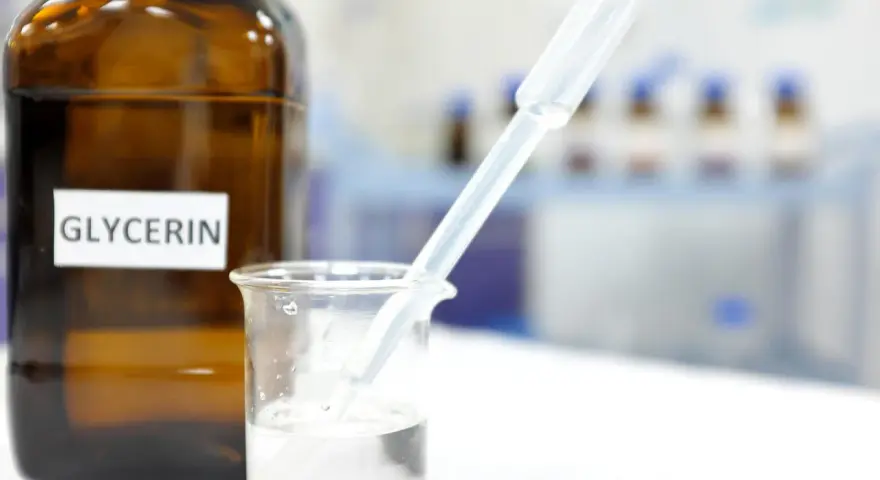 Braunglasflasche mit der Aufschrift "Glycerin". Ein Pipette tropft in ein Becherglas mit klarer Flüssigkeit, was die Glycerin verwendung in der Forschung zeigt.