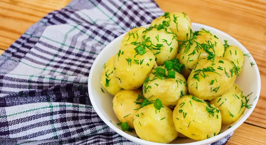 Młode ziemniaki w misce, posypane koperkiem i szczypiorkiem. Idealne na lato, a ile gotować młode ziemniaki? Krótko!
