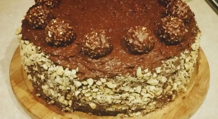 Pyszny tort ferrero rocher, oblany czekoladą i ozdobiony orzechami oraz kulkami.