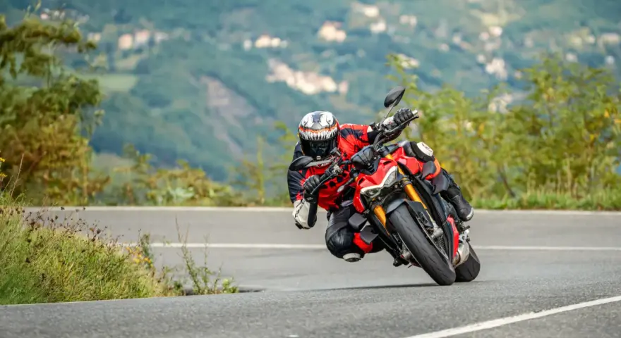 Un motociclista esperto piega in una curva stretta, con il ginocchio quasi a terra, affrontando un passo in montagna.