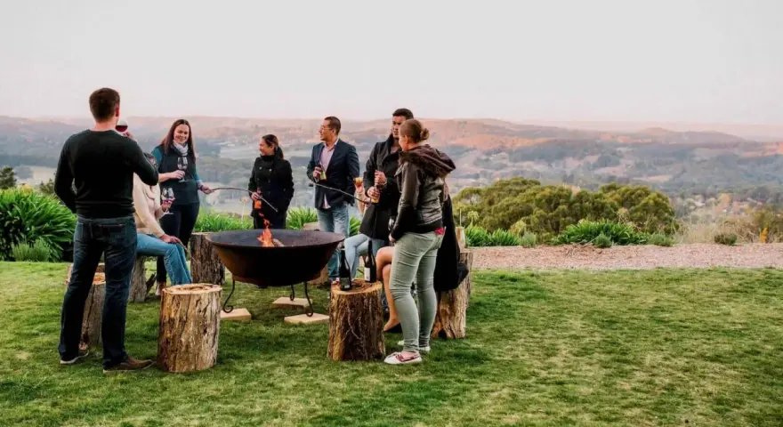 Staff retreat ideas for nonprofits: A group enjoys a bonfire and drinks outdoors, surrounded by rolling hills.