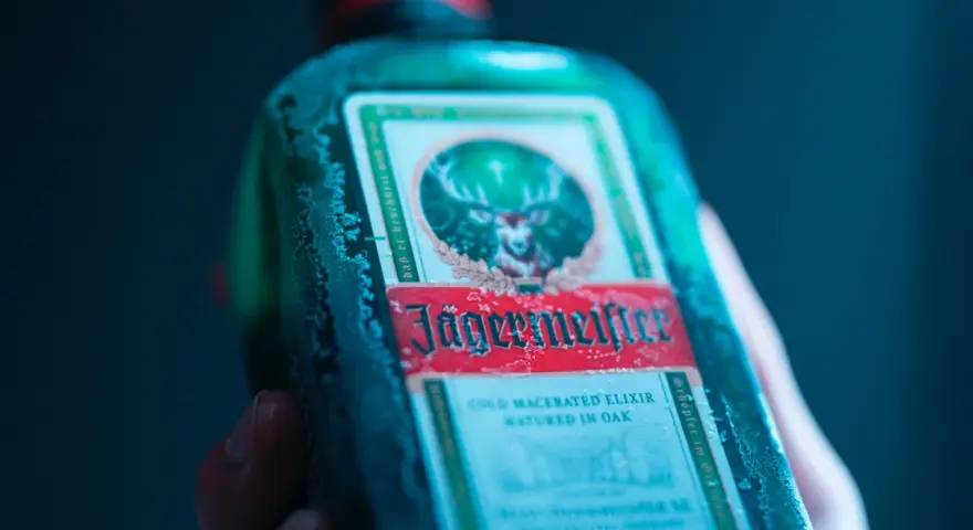 Zimna butelka Jägermeistera, znanego jako "zimny macerowany eliksir dojrzewający w dębie", z charakterystycznym jeleniem na etykiecie.