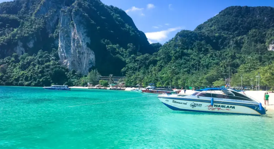 Turkusowa woda i łodzie motorowe przy plaży w Maya Bay. W tle zielone, skaliste góry.