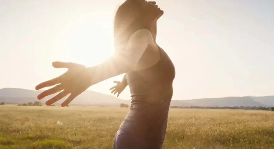 Frau mit ausgebreiteten Armen im Sonnenlicht, ein Symbol für das Heilen von Hypochondrie und das Finden von innerem Frieden.