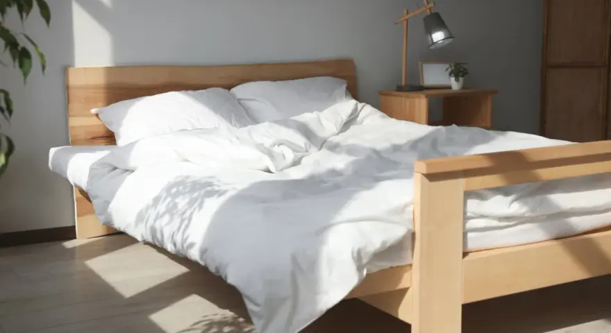 Ein helles Holzbett mit weißer Bettwäsche, das man leicht selber bauen kann. Sonnenschein fällt durch das Fenster.