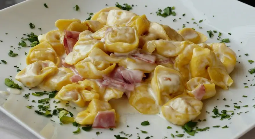 Tortellini panna e prosciutto, un classico piatto italiano, serviti su un piatto bianco con prezzemolo tritato.