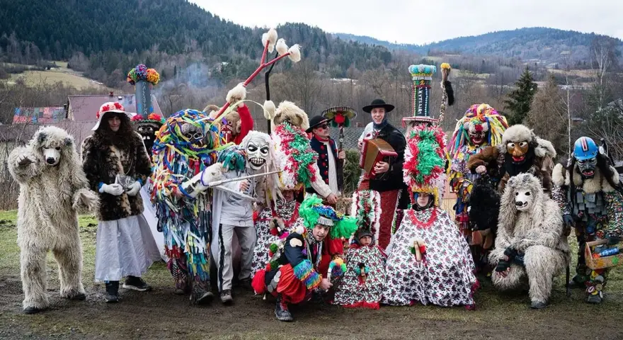 Kolorowy zwyczaj ludowy nowe latko: ludzie w fantastycznych strojach i maskach, niedźwiedzie, diabły i inne postacie pozują do zdjęcia na tle gór.