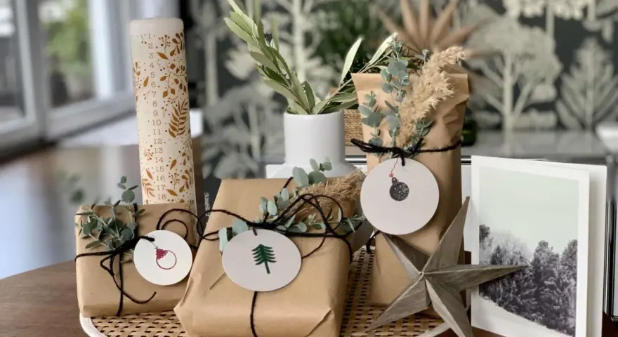 Schöne Geschenk verpacken Ideen: Geschenke in braunes Papier, mit Zweigen und Anhängern dekoriert, neben einer Adventskerze und einer Weihnachtskarte.