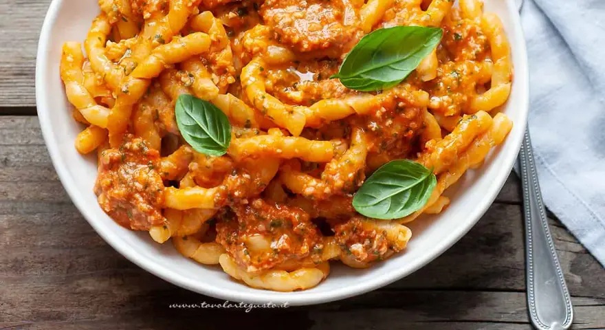 Un piatto invitante di busiate alla trapanese, condite con un sugo rosso e guarnite con foglie di basilico fresco.