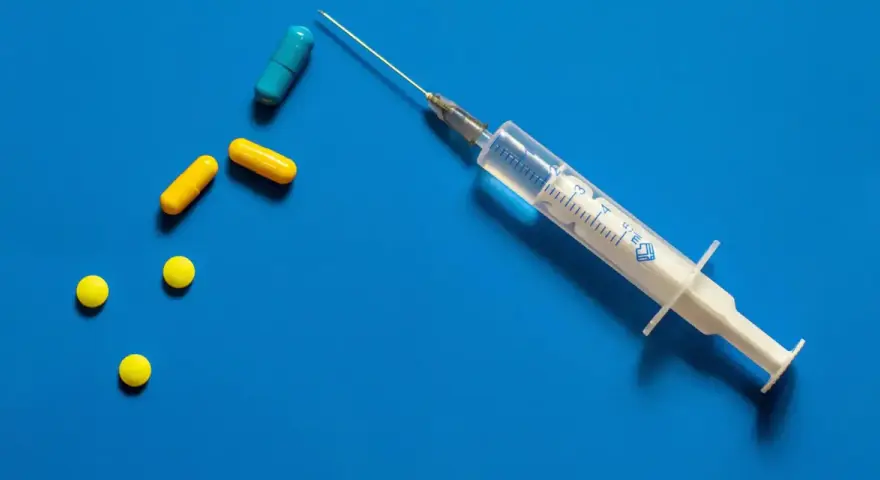 Strzykawka z igłą i kilka tabletek, w tym kapsułki. Może to być przygotowanie do zastrzyku hormonalnego.