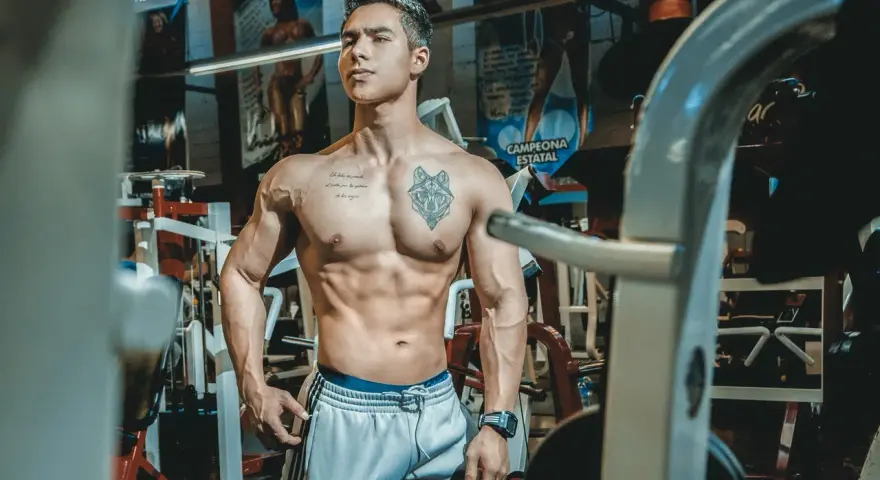 Muskulös man med tatueringar i gym. Han har en imponerande fysik, ett resultat av hårt arbete och att **deffa mat**.