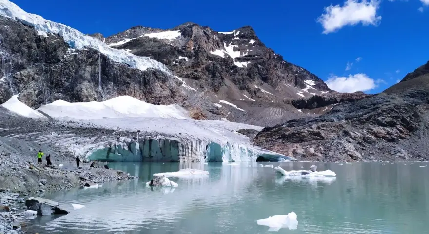 Un lago glaciale riflette montagne imponenti e il ghiacciaio Fellaria, con iceberg che galleggiano sull'acqua turchese.