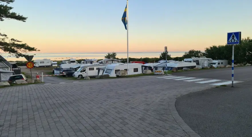 Solnedgång över Lerbergets camping med husbilar och husvagnar uppställda. En svensk flagga vajar i vinden.