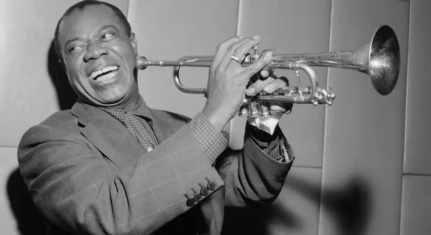 Louis Armstrong, znany jako "Satchmo", gra na trąbce z charakterystycznym uśmiechem.