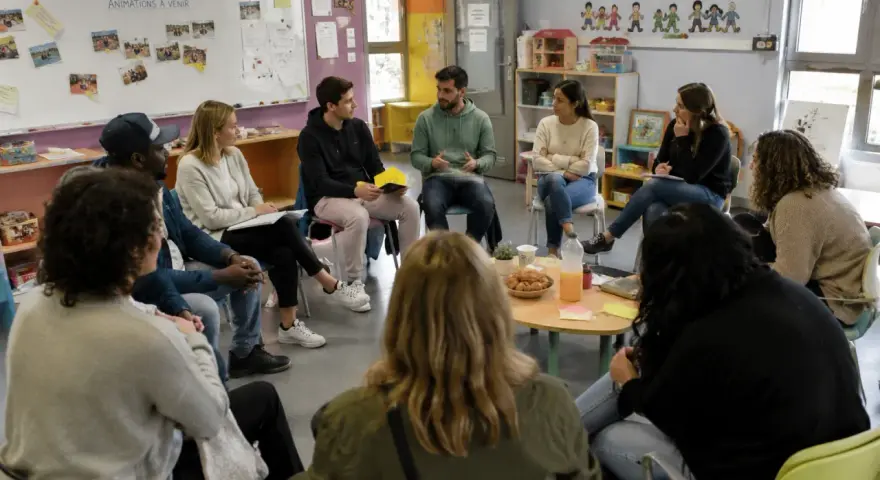 Des participants échangent lors d'une formation, peut-être des stages BAFA, dans une salle colorée.