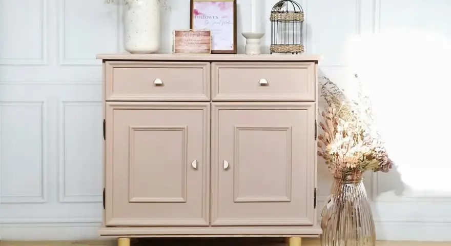 Meuble ancien repeint en rose poudré, avec deux tiroirs et deux portes. Décoré de fleurs séchées et d'une cage à oiseaux.
