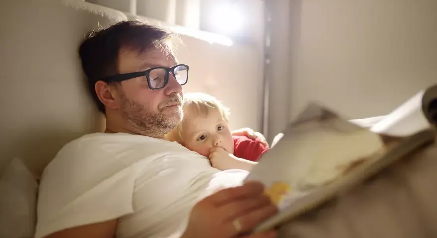 Vater im Elternzeit, 1 Monat alt, liest seinem Kind im Bett eine Geschichte vor.