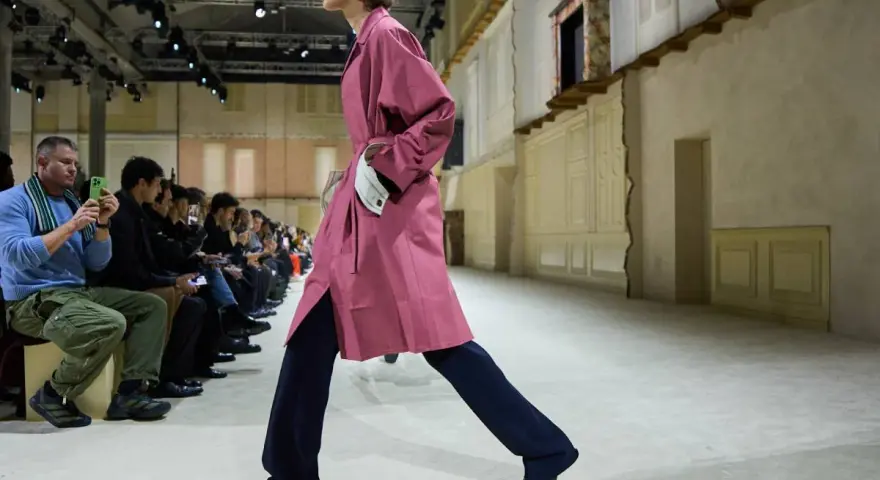 Modello sfila con trench rosa e pantaloni blu, un esempio di moderno stile uomo.