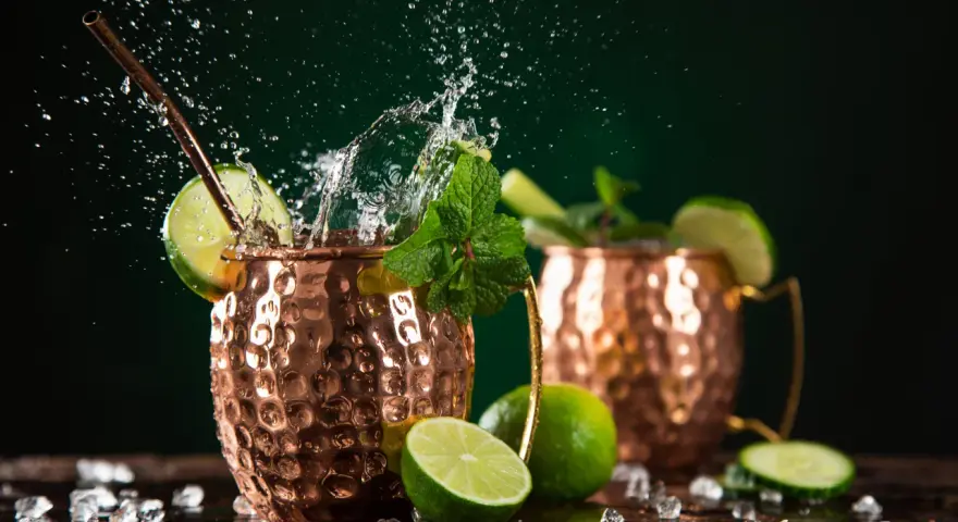 Dwa miedziane kubki z Moscow Mule i London Mule, ozdobione limonką i miętą, z bryzgami wody i lodem.