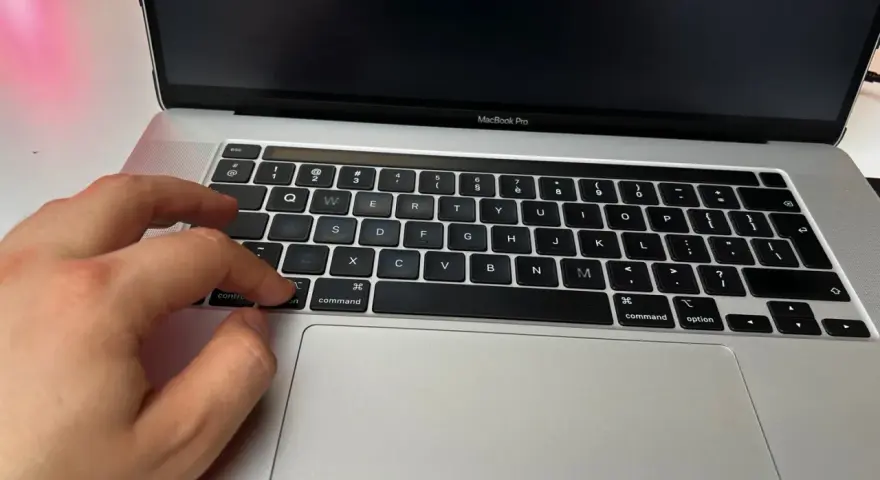 Dłoń naciska klawisz "command" na klawiaturze MacBooka, przygotowując się do instalacji drukarki.