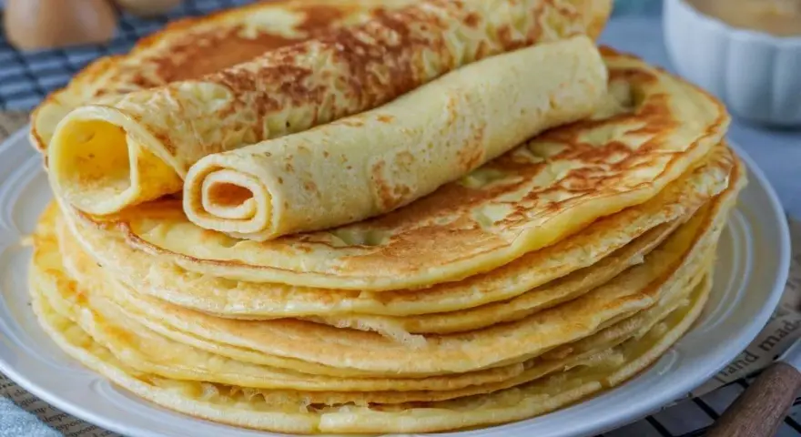 Ein Stapel goldbrauner Eierkuchen, zwei davon gerollt, perfekt für ein einfaches Eierkuchen Rezept.