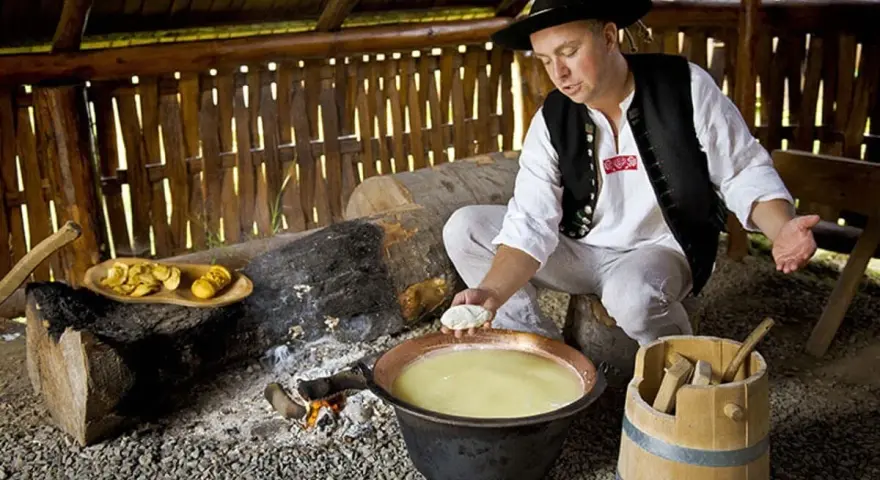 Uomo in abito tradizionale polacco prepara un prodotto tipico della Polonia: formaggio in un paiolo di rame.