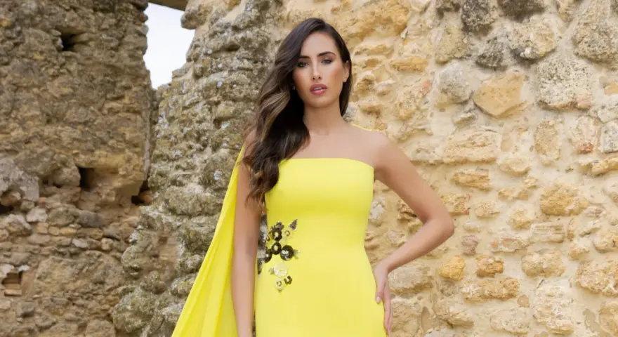 Mujer con vestido amarillo sin tirantes, con detalles florales y capa. Explora los diversos tipos de cuellos de vestidos.