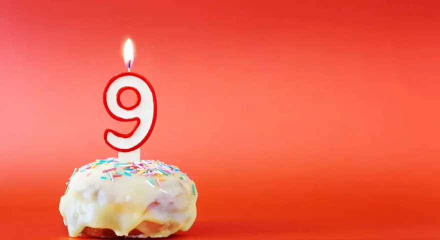En söt donut med vit glasyr och strössel, toppad med en brinnande ljusformad siffra nio. Perfekt för ett kalas för en 9-årig kille!