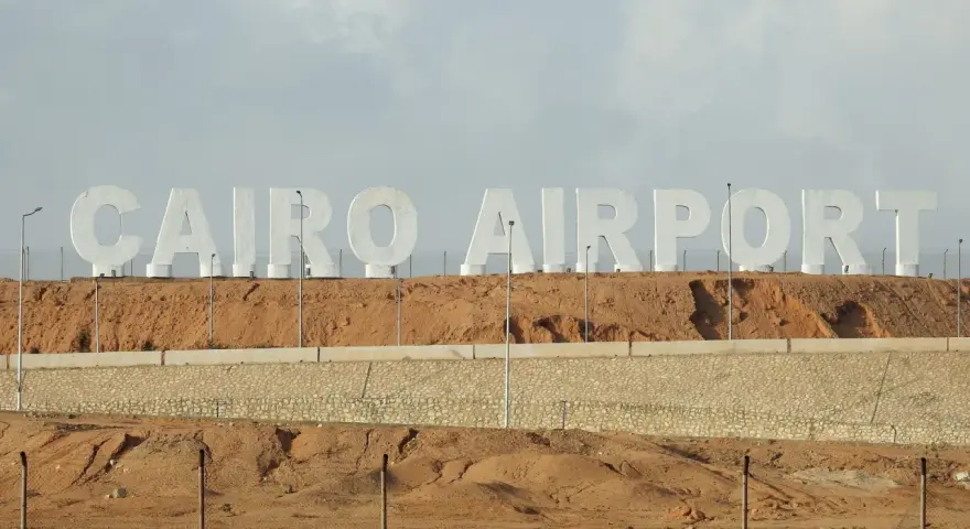 Ogromne białe litery "CAIRO AIRPORT" na tle pustynnego krajobrazu. Jedno z lotnisk w Egipcie.