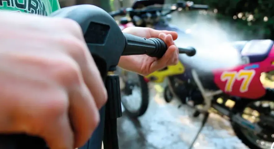 Mani che impugnano un'idropulitrice per pulire una moto da cross. Un modo efficace per capire come lucidare la moto.