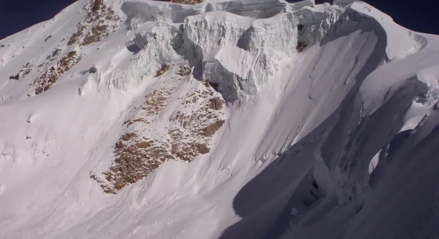 Schneebedeckte Gipfel des Huayna Potosí, mit steilen Eiswänden und felsigen Hängen unter einem tiefblauen Himmel.