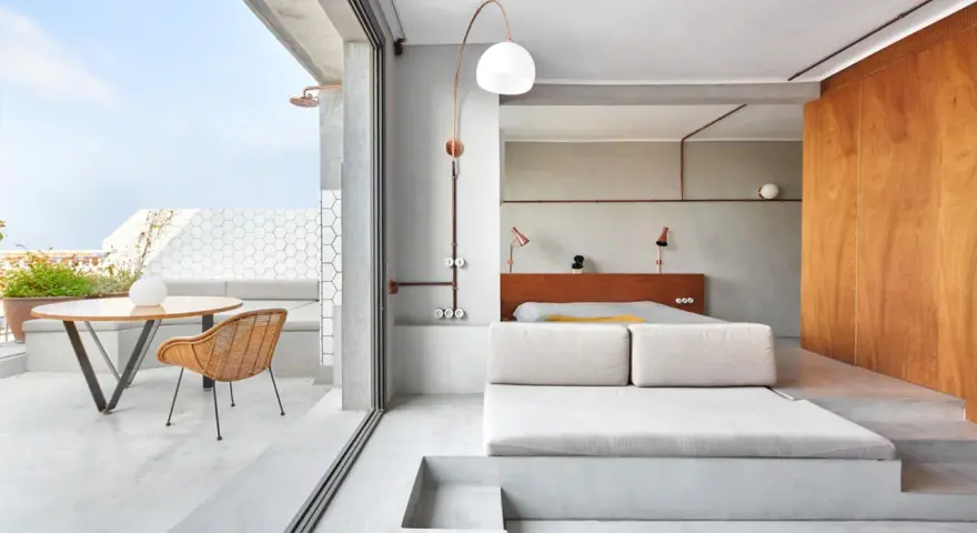 Habitación con diseño industrial, cama baja, sofá de lino y terraza con ducha exterior.