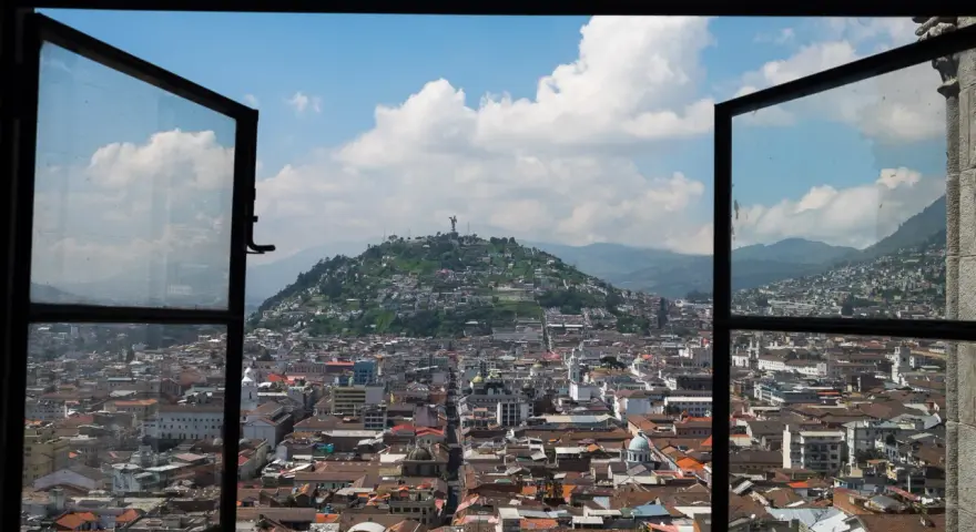 Widok na miasto z otwartego okna, z wzgórzem i pomnikiem w tle. To piękna panorama stolicy Ekwadoru, ze stolicą w Quito.