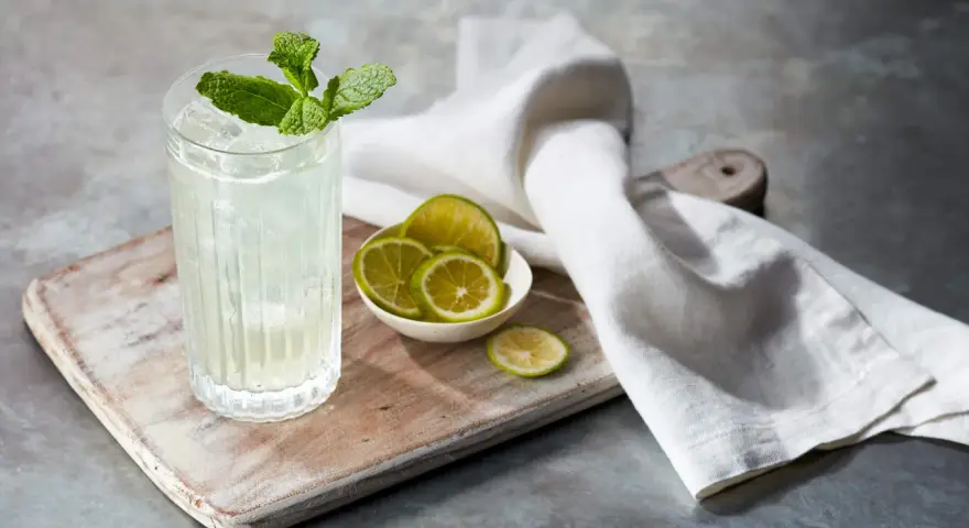 Orzeźwiający mojito z ginem, udekorowany miętą i podany z plasterkami limonki na drewnianej desce.
